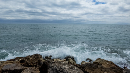 Tranquil seascape with waves crashing against rocky shoreline under a cloudy sky, ideal for travel and nature themes, related to World Oceans Day