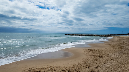 Serene sandy beach landscape with gentle waves under a cloudy sky, ideal for travel and summer vacation concepts