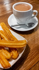 Cup of hot chocolate with freshly made churros on a wooden table, traditional Spanish breakfast or snack, related to Dia de la Hispanidad celebrations