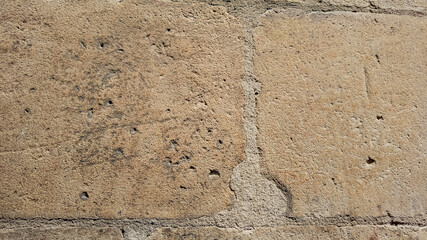 Close-up texture of a beige sandstone wall with visible grains and erosion, ideal for backgrounds in architectural or geological design concepts