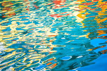 Colorful reflections on water creating an abstract pattern with vibrant hues of blue, yellow, red, and green.