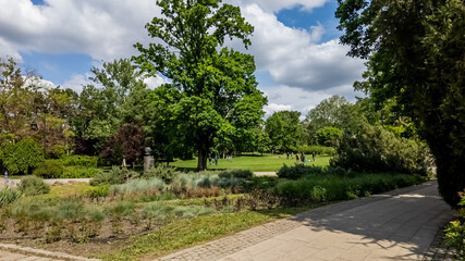 Tranquil city park with lush green trees, walking paths, and visitors enjoying a sunny day, ideal for Earth Day or outdoor leisure themes