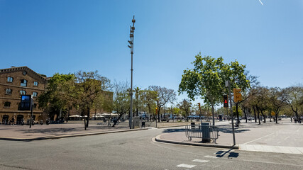 Sunny urban square with lush green trees, traffic lights, and a surveillance camera pole on a clear...