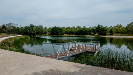 Serene park pond with floating metal pier on a cloudy day, perfect for environmental themes,...