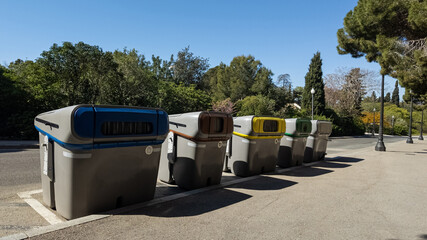 Row of various colored recycling bins in a park, symbolizing environmental conservation and waste management, related to Earth Day and sustainability initiatives