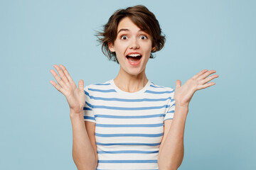 Fototapeta premium Young surprised shocked excited fun woman she wear striped t-shirt casual clothes look camera spread hands isolated on plain pastel light blue cyan color background studio portrait. Lifestyle concept.