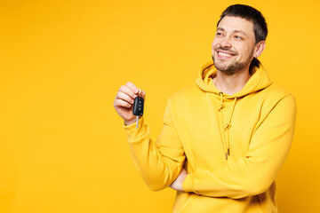 Young smiling happy Caucasian man wears hoody casual clothes hold in hand car keys fob keyless system look aside on area isolated on plain yellow orange background studio portrait. Lifestyle concept.