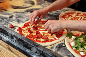 Closeup image of pizzamaker spreading pepperoni on pizza dough