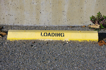 LOADING sign on yellow concrete curb stop parking block