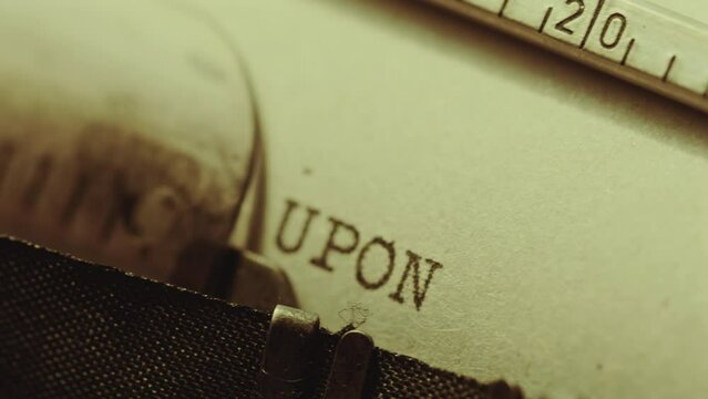 Typing Once Upon a Time phrase in capital letters on page of paper while writing a fairytale with analog typewriter. Extreme close-up shot