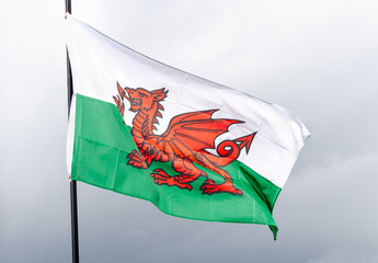 The Welsh flag featuring a red dragon on a green and white background waving against a cloudy sky. Suitable for cultural or national pride content.