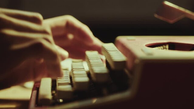 Hands of unrecognizable writer or journalist working on vintage typewriter at desk. Close-up shot, side view