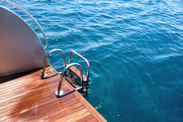 Back teak wooden deck and metal ladder of a of motor yacht over the sea.