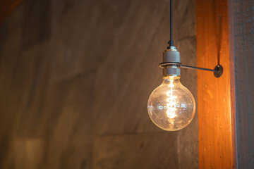 A classic designed tungsten lightbulb is glowing in orange warmlight shade with blurred background of building interior. Close-up and selecitve focus.