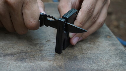 Fototapeta premium Man is sharpening a survival knife using a knife sharpener outdoors