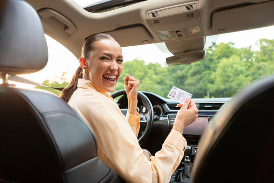 Overjoyed European lady sitting in her own car and holding new driver license, celebrating driving school finish, sitting inside of vehicle