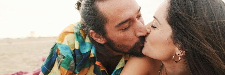 Couple in love lies and kissing on the beach and taking a selfie on mobile phone, panorama