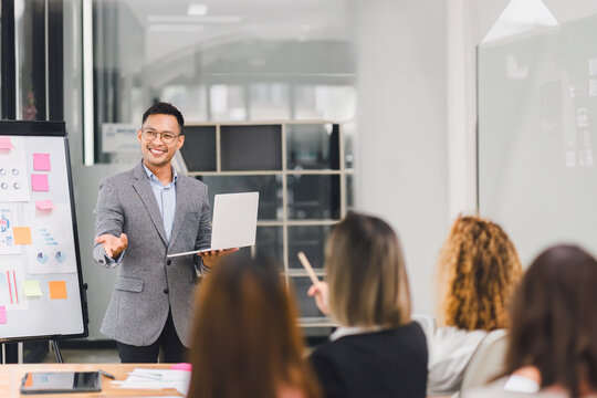 Confident businessman leading a meeting, engaging with colleagues while presenting data charts and graphs in a modern office.