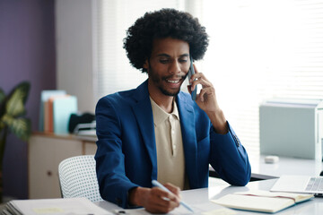 Smiling businessman taking notes when talking on phone with colleagues