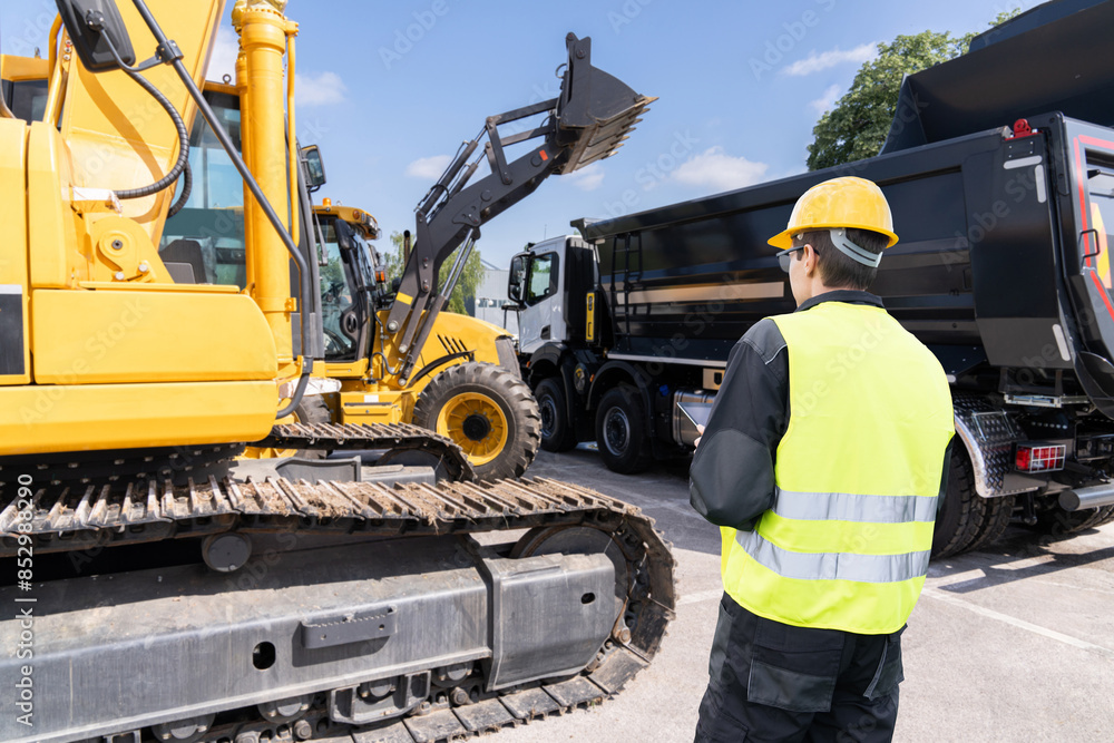 Aufkleber engineer in a helmet with a digital tablet stands next to construction excavators