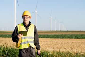 Engineer with digital tablet works on a field of wind turbines