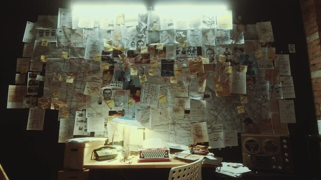 Police officer workplace with retro typewriter and telephone under large evidence board full of printed criminal investigation materials connected by strings in the office at night