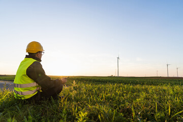 Worker sits on the grass and looks at wind turbines