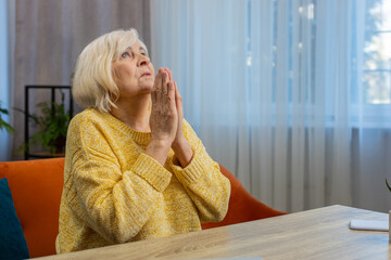 Please, God help. Worried senior woman praying for heath sincerely with folded arms, looking upward...