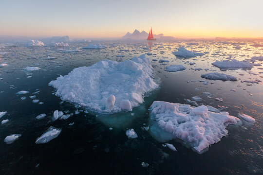 Rad sailing boat among icebergs at sunset  in Ilulissat Icefjord, Greenland