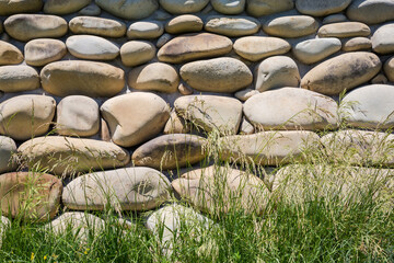 Wall faced with natural boulders with high grass on foreground