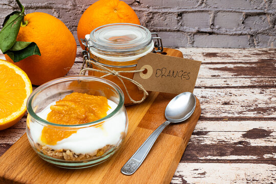 Glass jar full of muesli and yogurt with homemade orange jam, delicious snack with cheesecake and orange jam on wooden cutting board, detail with vintage cardboard tag