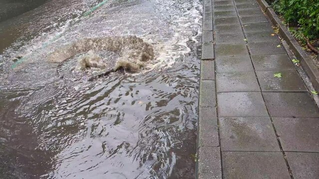 Water lifting an iron sewage manhole cover on the road, strong water pressure flowing onto the roadway. Impromptu flooding after heavy rain, drainage systems overwhelmed by the force of nature.