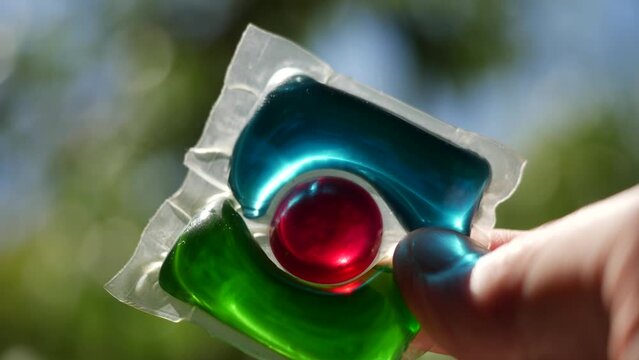 Laundry detergent pod. Men hand holds colorful water soluble sachet. Packs or liquitabs are water-soluble pouches containing highly concentrated laundry detergent, softener and other laundry products