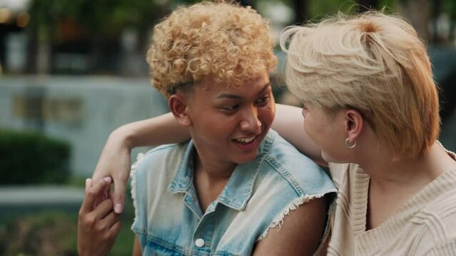 Asian guy with curly hair laughs talking to romantic partner in city park closeup. Gay couple talks having fun in urban garden. LGBTQI community support and acceptance in pride month