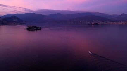 Lake Maggiore Aerial View: The serene expanse of a calm lake reflects the soft hues of the twilight sky, with silhouetted mountains and a distant island enhancing the tranquil atmosphere.