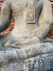 Close-up of stone Buddha statue's torso and hand on lap, detailed and weathered textures, brick wall