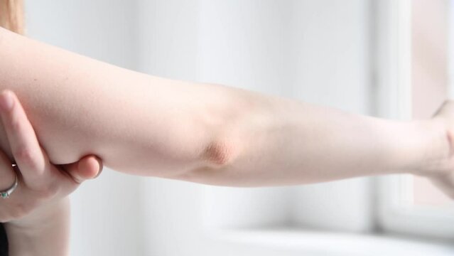 Close-up view of woman rubbing her elbow against light roomwall. Real time handheld video. Soft focus. Healthcare, cosmetics and self massage theme.