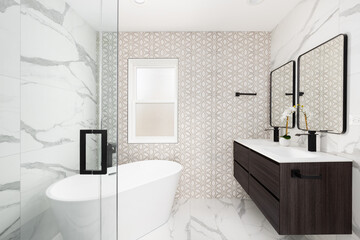 A bathroom with a brown and white pattern tiled accent wall, marble flooring and walls, floating wood cabinet, and freestanding soaking tub. No brands or labels.