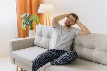 Young man suffering from headache at home, touching his temples, copy space, blurred background....