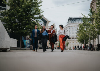 Four business professionals walking together on an urban street, engaging in casual conversation with smiles and business attire.