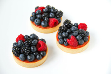 French dessert. Three berry tarts are decorated with organic fresh blueberries, raspberries and blackberries. White background. Back view. 