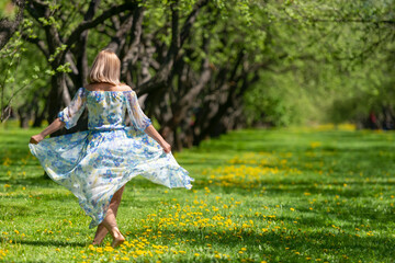 Slender girl in a dress dancing barefoot on the grass and flowers in the spring garden