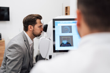 Attractive male doctor ophthalmologist is checking the eye vision of handsome middle age man in...
