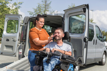 Female assistant helping a man in a wheelchair to use a smartphone. Disability and daily activity...