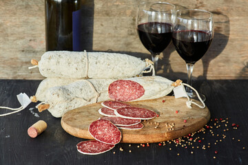 Smoked sausage with white mold on a wooden table surrounded by spices and two glasses of red wine. Meat production