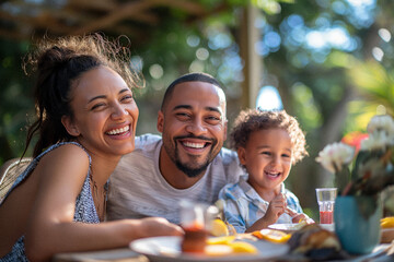 A diverse young family enjoying a summer day being outside together eating lunch in their beautiful backyard laughing with each other. Themes of unity, happiness and family