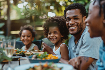 A diverse young family enjoying a summer day being outside together eating lunch in their beautiful backyard laughing with each other. Themes of unity, happiness and family
