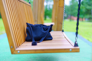 Forgotten black fabric bag resting on wooden swings, a quiet moment of absence
