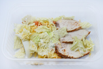 Caesar salad with meat and vegetables in a plastic container. A light breakfast.