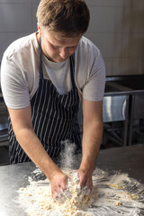 A man chef in an apron prepares pasta in a restaurant kitchen. Kneads the dough with eggs. The process of preparing pasta dough. Noodles. Italian Cuisine. Recipe.